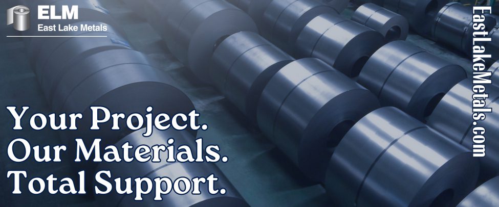 A series of large, dark grey architectural metal coils lined up in an industrial warehouse facility belonging to a premier metal roofing supplier in Northwest Indiana.