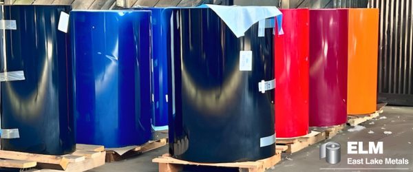 A side view of a blue industrial forklift lifting a massive roll of white pre-painted metal coil inside a manufacturing warehouse, showcasing the logistical capabilities of a metal roofing supplier in Northwest Indiana.