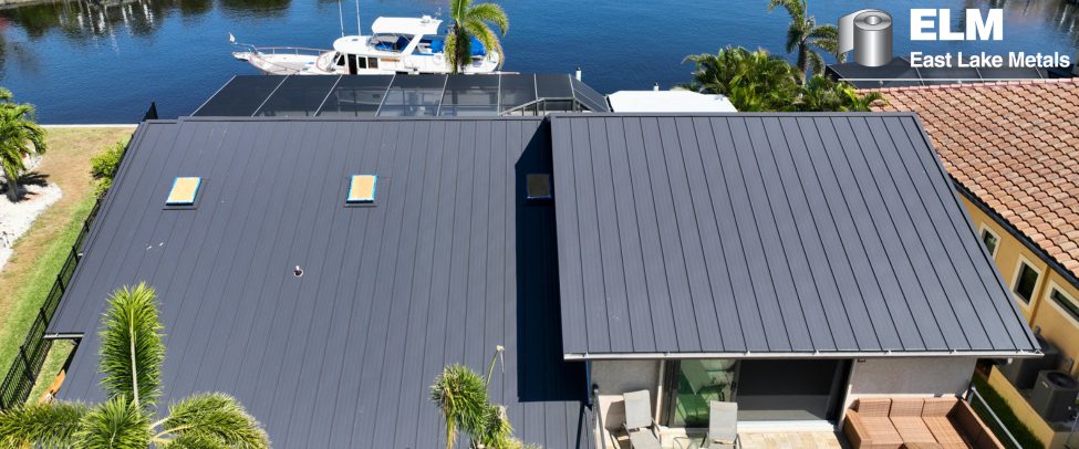 High-angle aerial view of a beachfront home featuring a dark gray standing seam metal building envelope by East Lake Metals, demonstrating the durability of Armored Coast Roofing in Florida.