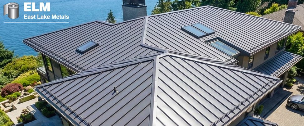 High-angle aerial view of a luxury waterfront home featuring a complex dark gray standing seam metal roof, demonstrating the aesthetic and protective benefits of PVDF coatings from East Lake Metals.