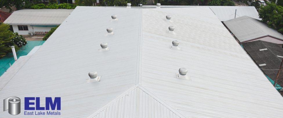 High-angle aerial view of a wide-span commercial metal roof equipped with ridge turbine vents, optimized with solar-reflective UV resistant coatings from East Lake Metals.