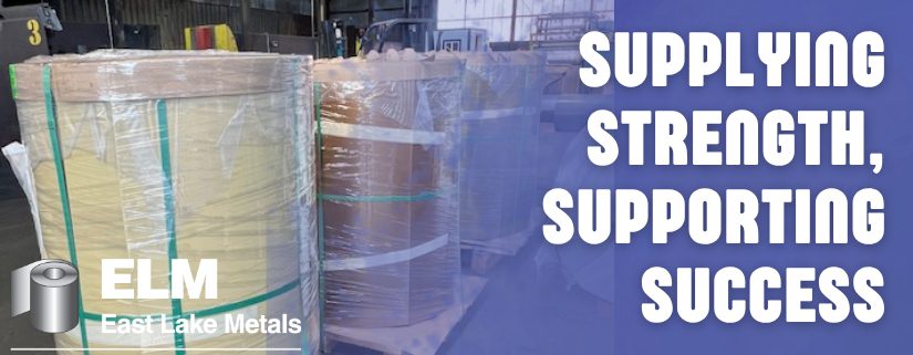East Lake Metals banner titled "SUPPLYING STRENGTH, SUPPORTING SUCCESS," featuring high-capacity steel coils wrapped for transport in a warehouse to demonstrate their role as a trusted metal supplier for industrial manufacturing.