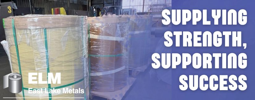 East Lake Metals banner titled "SUPPLYING STRENGTH, SUPPORTING SUCCESS," featuring high-capacity steel coils wrapped for transport in a warehouse to demonstrate their role as a trusted metal supplier for industrial manufacturing.